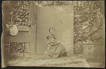 Alexine Tinne zittend voor een kamerscherm in de tuin van Lange Voorhout 32 te Den Haag; geheel links haar rijzadel. Foto door Alexine Tinne en assistent, juli 1860.