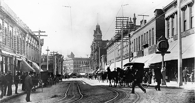 Harris & Frank's London Clothing Co., with its landmark clock, visible at far right in Allen Block. View south on Spring St. from Temple, c.1883–1894. The towers in the background are the Phillips Block; the two larger buildings to its right are the Jones Block and (with turrets) City of Paris.