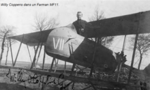 Photographie noir et blanc d'un homme debout dans le cockpit d'un biplan au sol.
