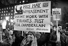 A woman holds a sign reading "Mrs May – appeasement doesnt work with tyrants. Just ask Chamberlain. #resist #muslimban