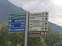 A post with signs to Gran San Bernardo, Aosta, the Via Francigena and local places in Quart. The text is in Italian and French.