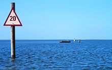 A small boat and wading fishermen in shallow water by a beach