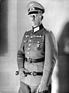 A man wearing a military uniform and peaked cap holding a baton.