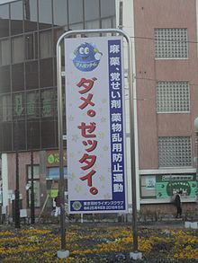 A roadside sign with a cartoon globe above a Japanese slogan in large bold text