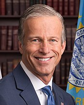 John Thune smiling in front of a South Dakota flag