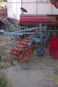 Ältere Hackmaschine mit Lenkung; auf dem Sitz hinten lenkt eine zweite Person die Hackmaschine, während jemand den Traktor durch die Reihen steuert