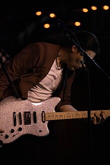 Guitar player performing with his custom built guitar that is covered in silver sparkles