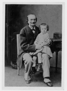 photograph of middle-aged father in frock coat, wearing Pince-nez eyeglasses and moustache, but no side-whiskers, with toddler sitting on his knee