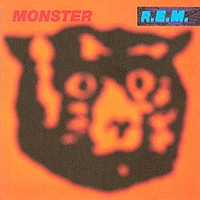 An album cover showing a blurred drawing of a bear's head in black against an orange background. The name of the album is in red text in the top-left corner of the cover and the band's name is in blue text on a black background in the top-right corner of the cover.