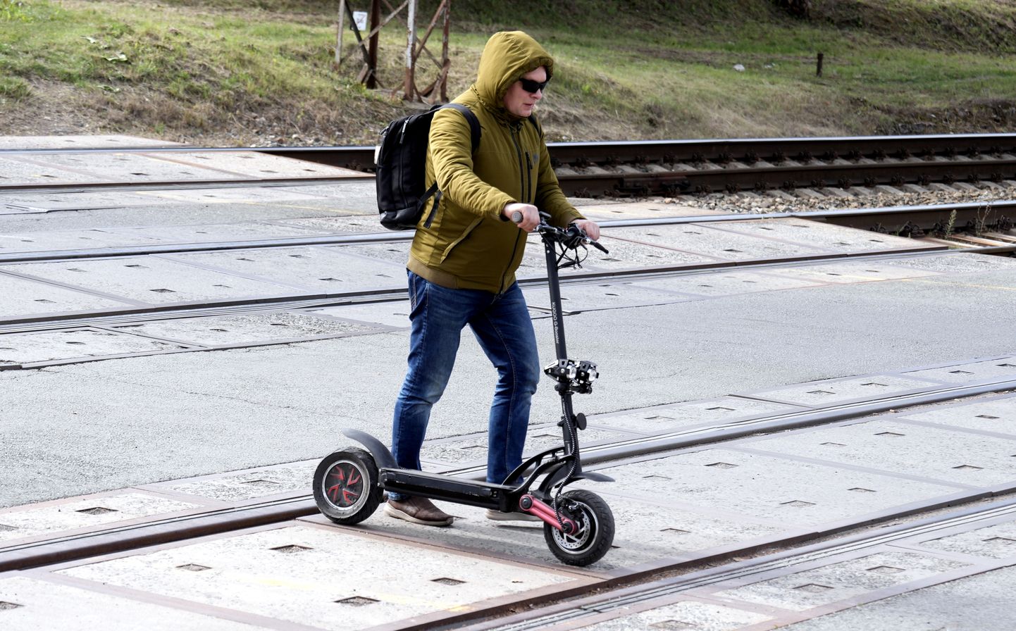 Vīrietis ar elektroskūteri šķērso dzelzceļa pārbrauktuvi Matīsa ielā.