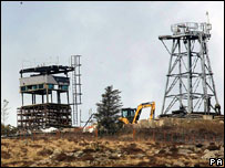 Digger on hill among watchtowers being dismantled