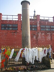 Ancient stone pillar surrounded by a small fence, covered with devotional clothes