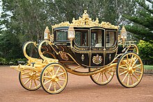 A very ornate coach, black with gold trim, a coat of arms on the door