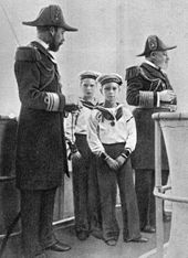Deux hommes âgés en uniforme d'officier naval et portant un bicorne entourent deux enfants en uniforme de matelot.