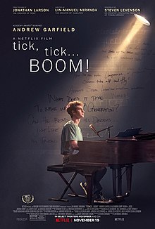 A young man sits at a piano with a spotlight shining on him