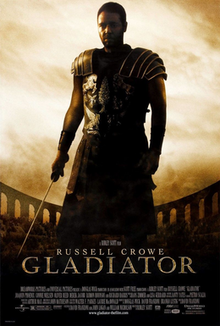 A man standing at the center of the image is wearing armor and is holding a sword in his right hand. In the background is the top of the Colosseum with a barely visible crowd standing in it. The poster includes the film's title and credits.