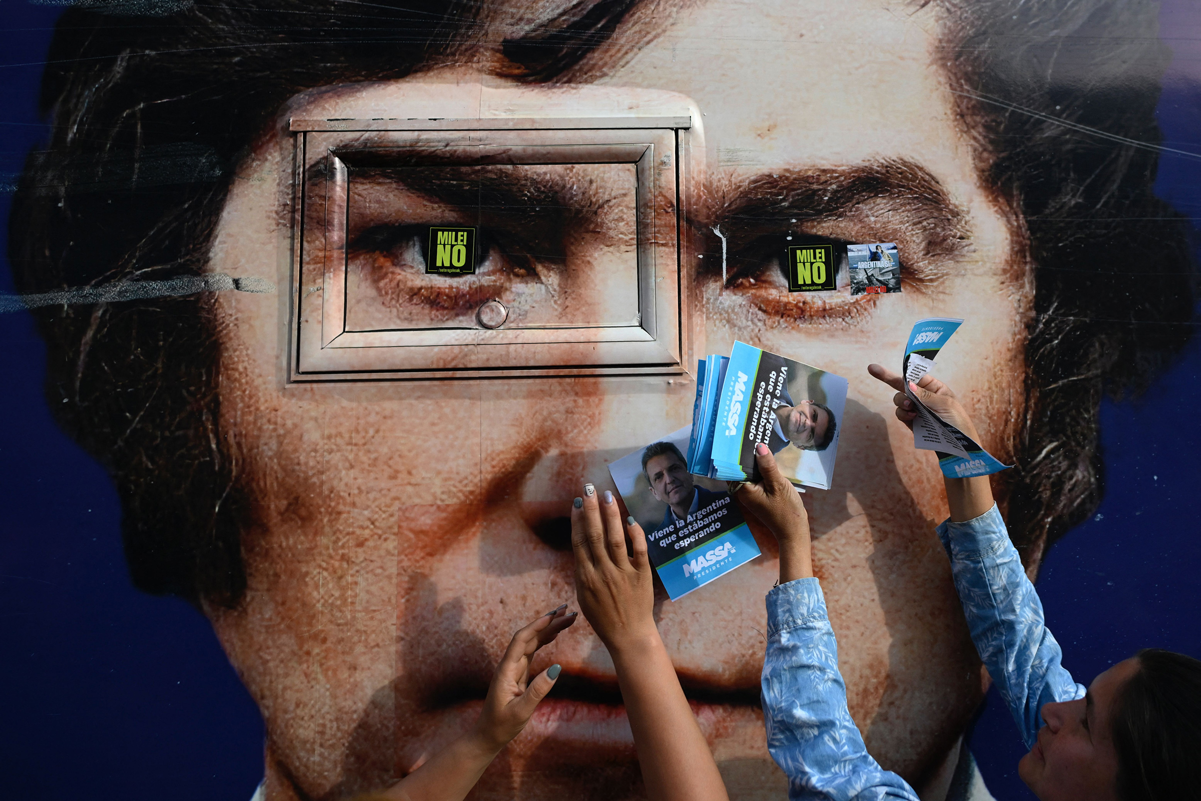 Supporters of Argentina's former Economy Minister and presidential candidate for the Union por la Patria party, Sergio Massa, hold posters of their candidate in front of an image depicting Milei, during Milei's campaign rally in Ezeiza in November. Elected for his economic vision, Milei is also fighting a broader cultural battle.