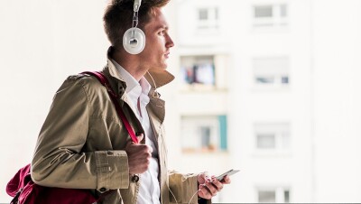 A stylishly dressed man listens to audio from his smartphone via headphones