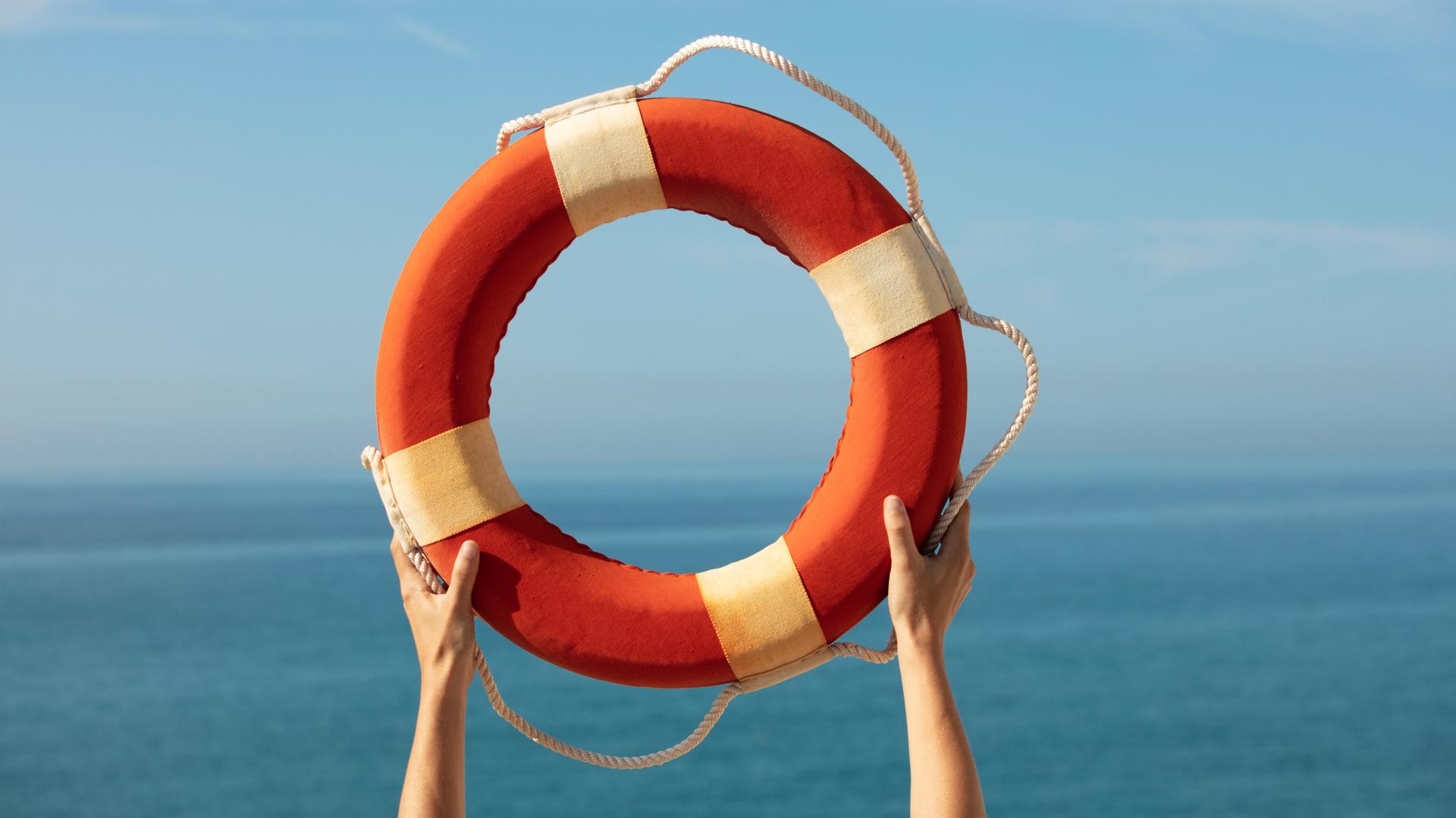 Hände halten einen Rettungsring vor blauem Himmel in die Luft.