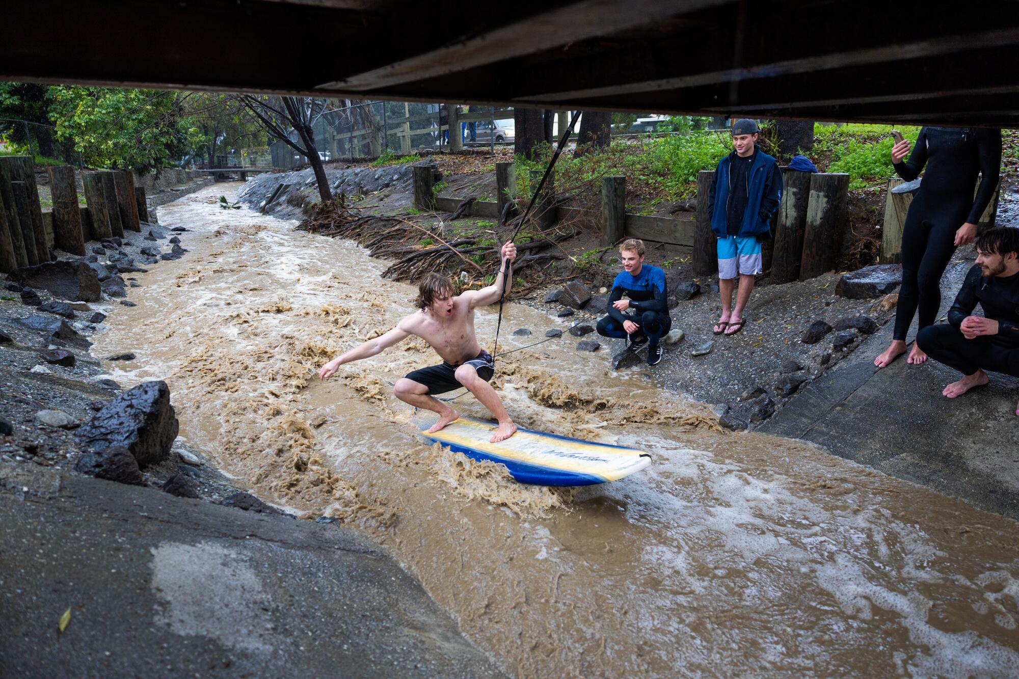 A man takes his turn using a rope from a footbridge to stay in position and surf stormwater.