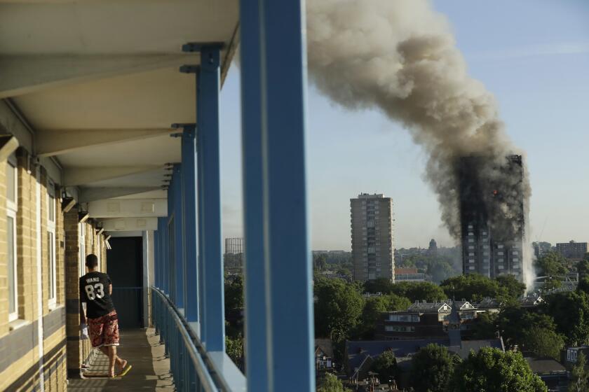 FILE - A resident in a nearby building watches smoke rise from the Grenfell Tower building on fire in London, Wednesday, June 14, 2017. (AP Photo/Matt Dunham, File)