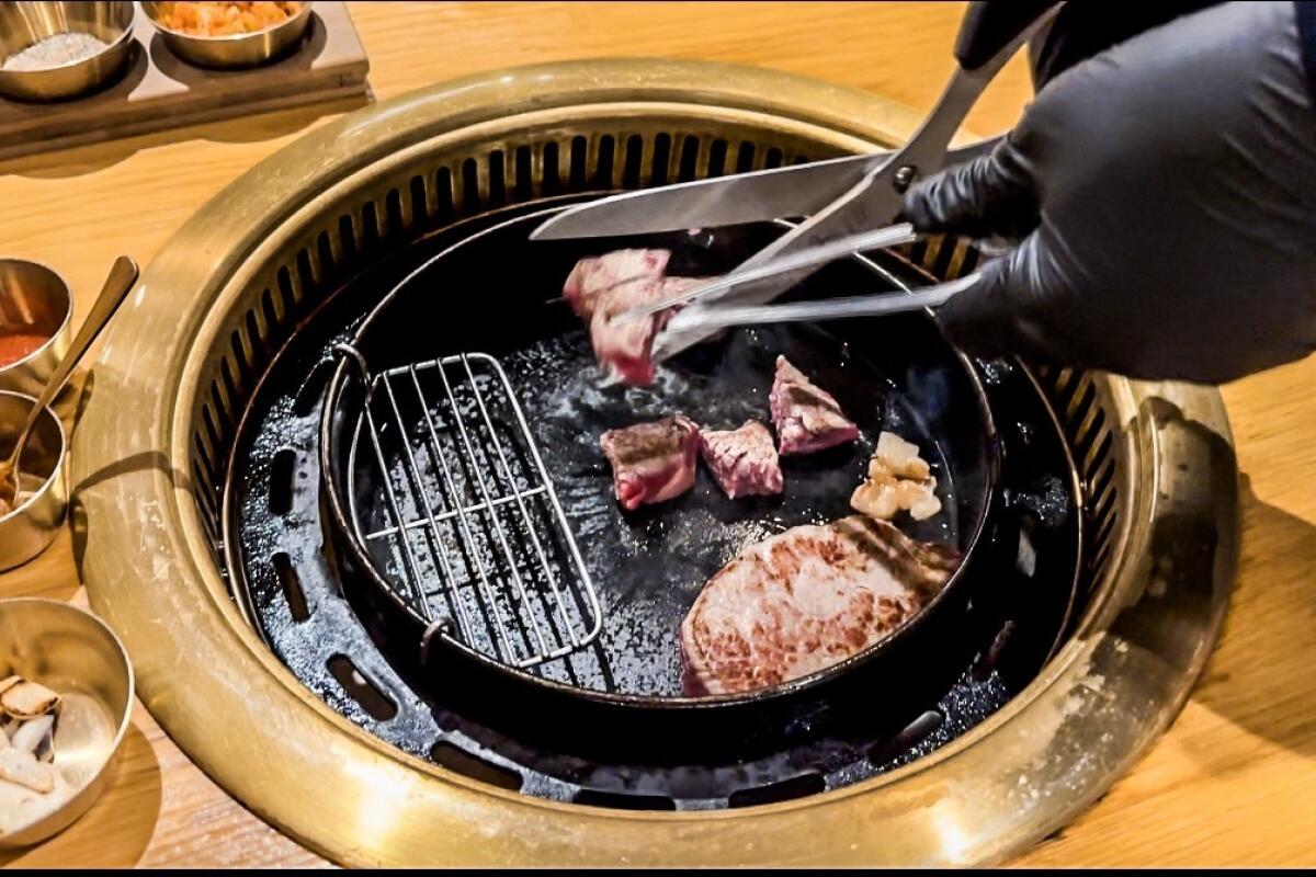 Staff cuts into ribeye meat as it cooks on an open grill at Daedo Sikdang.