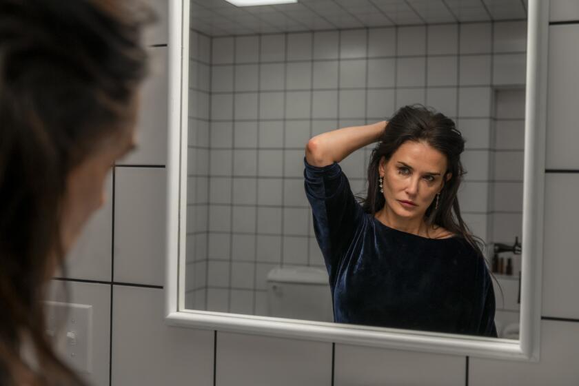 A woman runs her hand through her hair, looking in the mirror.