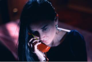 A woman listens to a voice on a red phone.