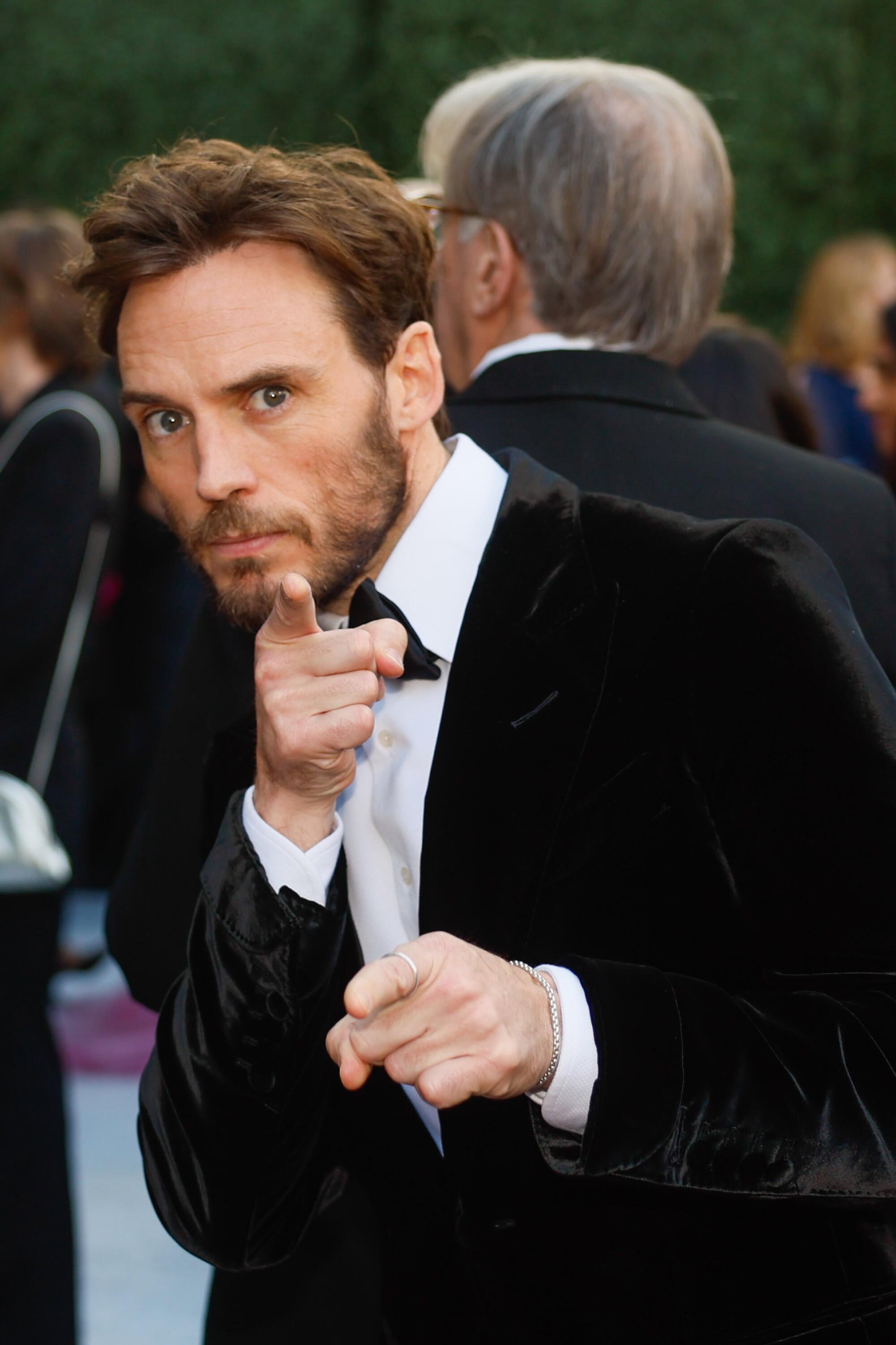 Sam Claflin points at the camera at the Emmy Awards.