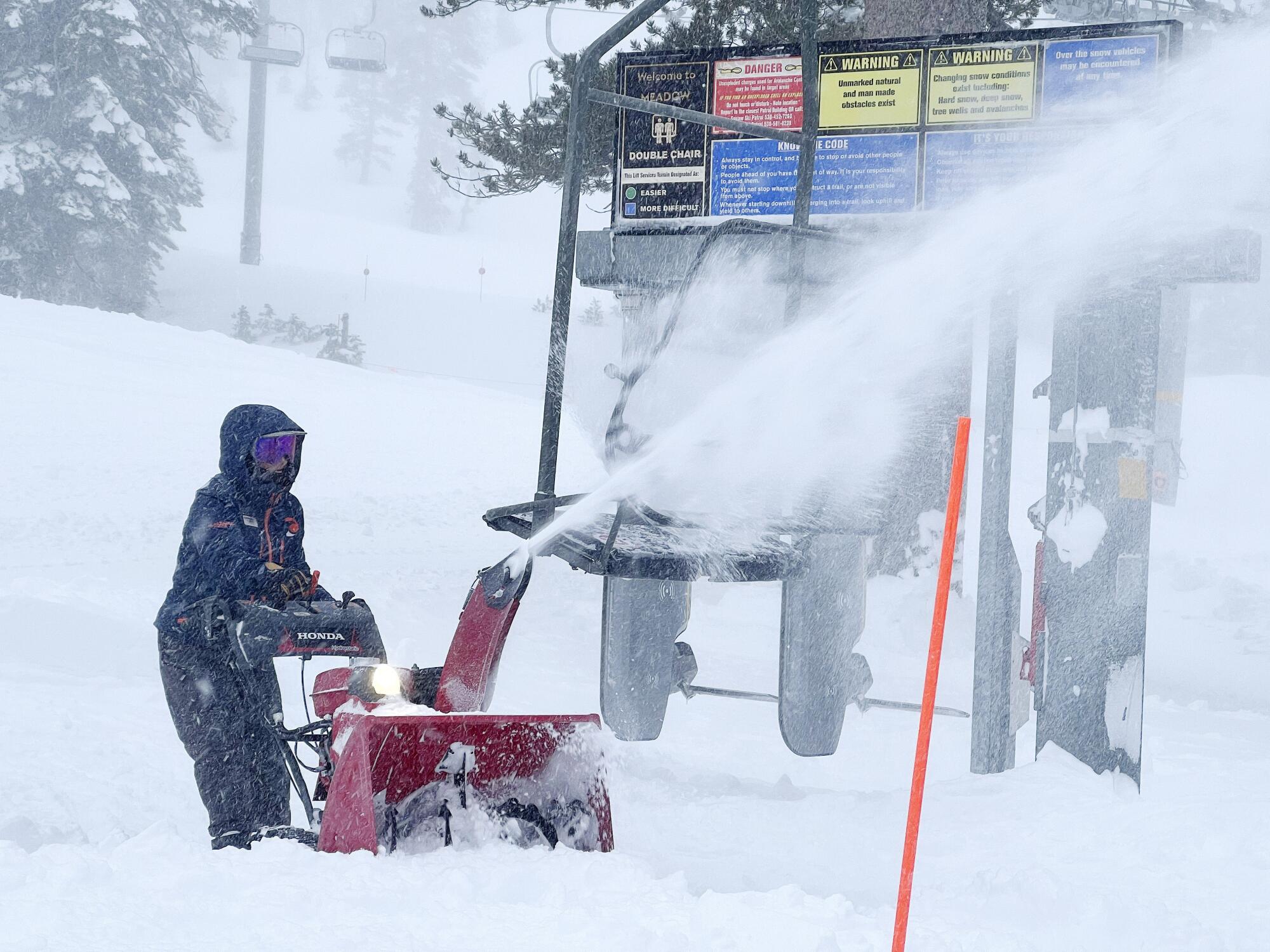 An employee uses a snow blower to clear snow at a ski resort near a ski lift chair.
