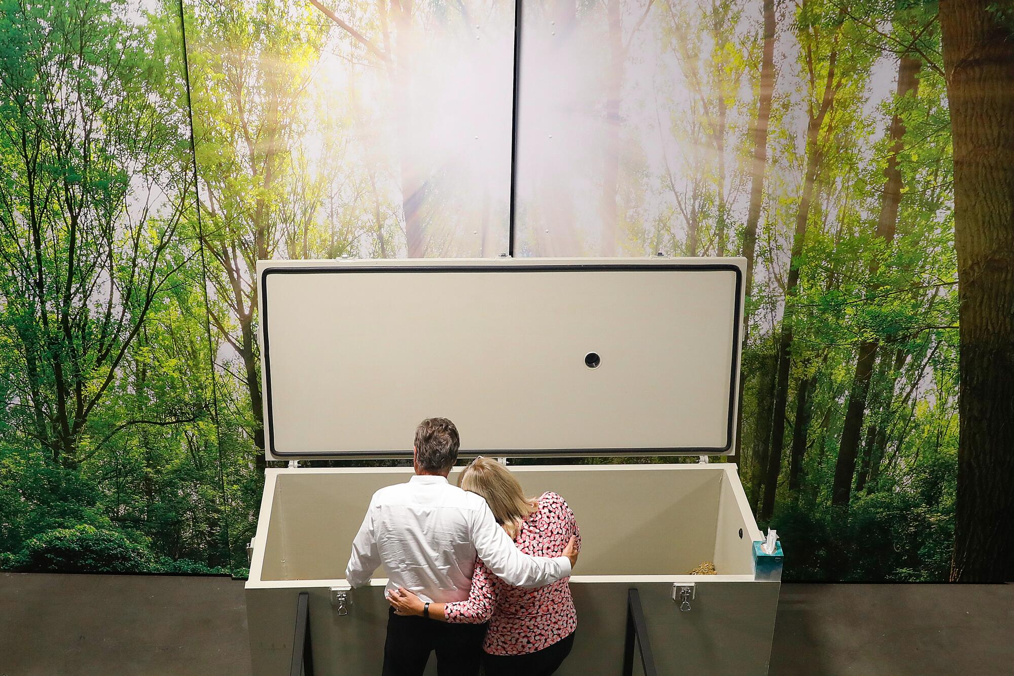 Heidi and Joe Heffington hug in front of a vessel holding Heidi's dead mother who will undergo human composting.