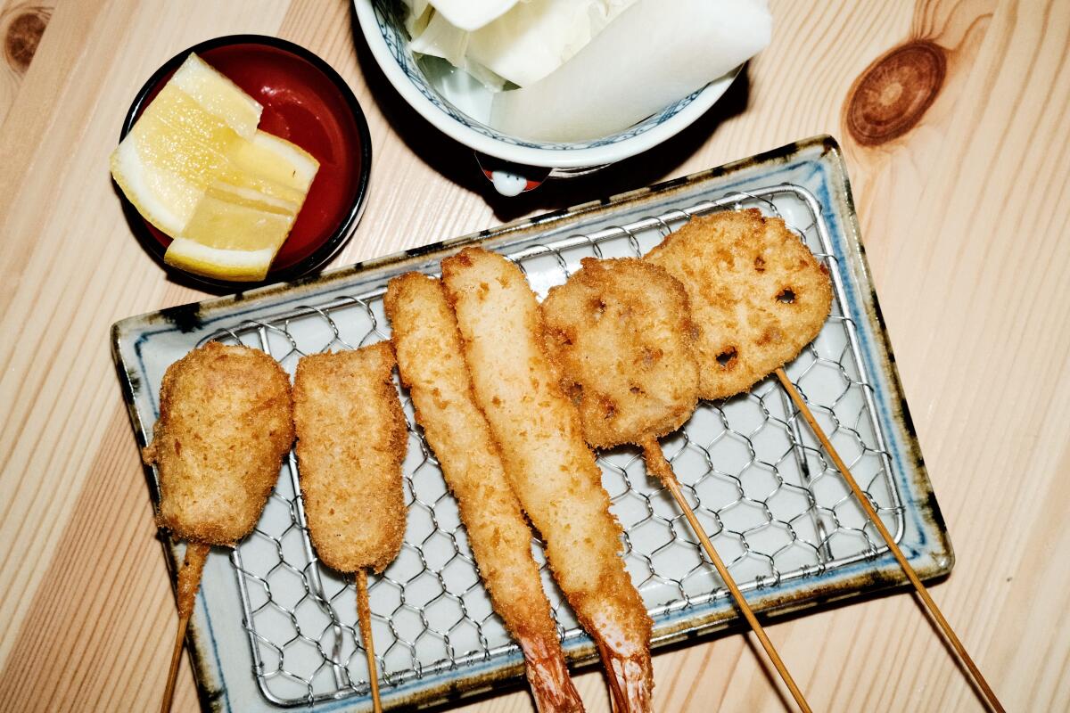 An overhead photo of an array of six kushikatsu, or fried skewers, on a ceramic plate at Japanese spot Kushiba in Echo Park.