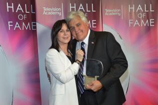 Mavis Leno wears a white blazer while embracing husband Jay Leno, who is holding a TV trophy