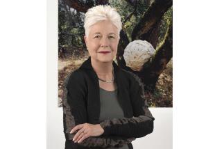 A woman with short white hair stands with her arms crossed in front of her