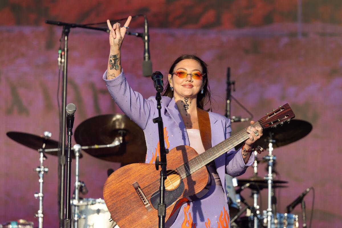 A guitarist raises her right hand in the rock horns symbol as she performs.