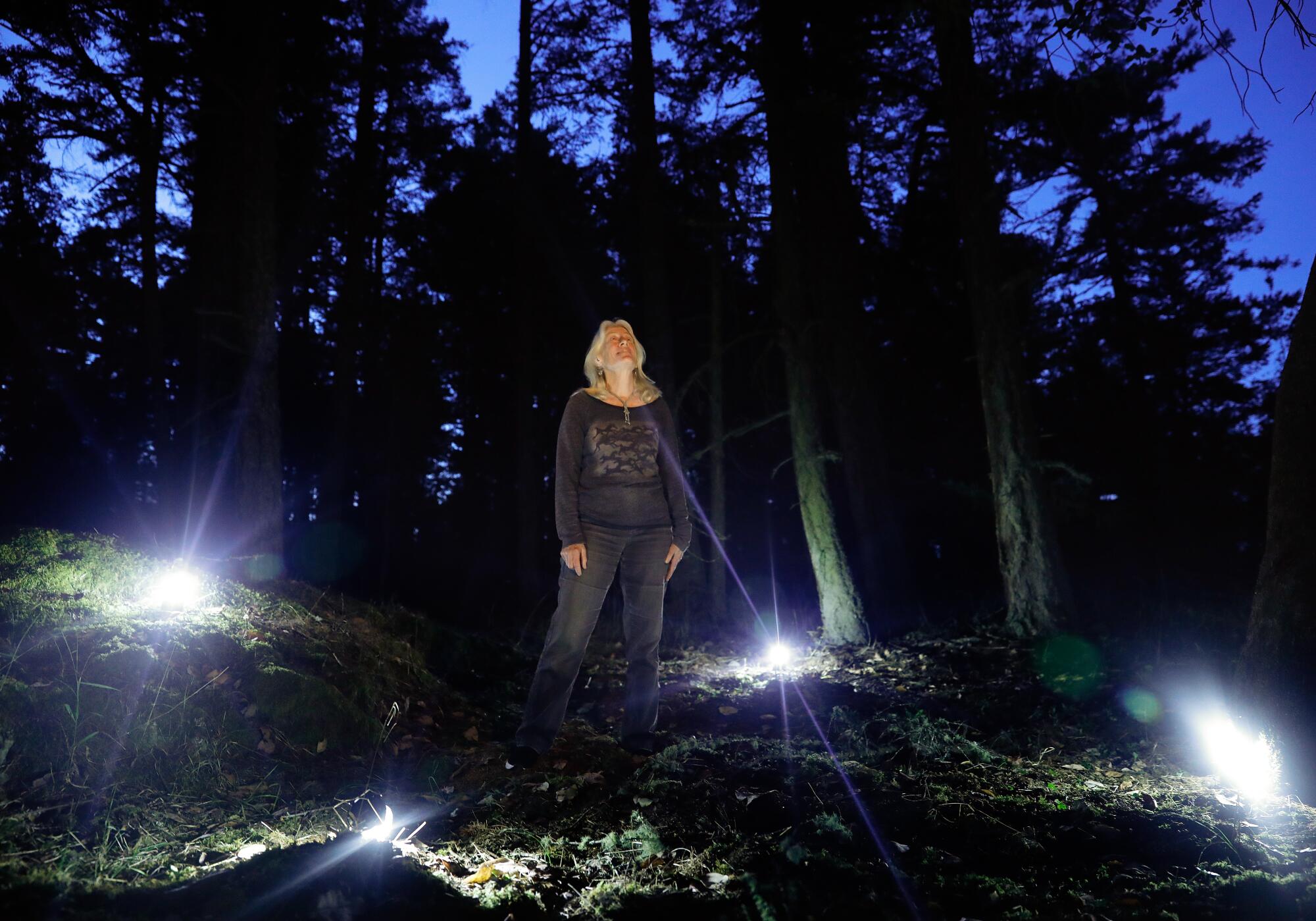 Blaire Van Valkenburgh surrounded by lanterns in the woods stares up into a darkening sky.