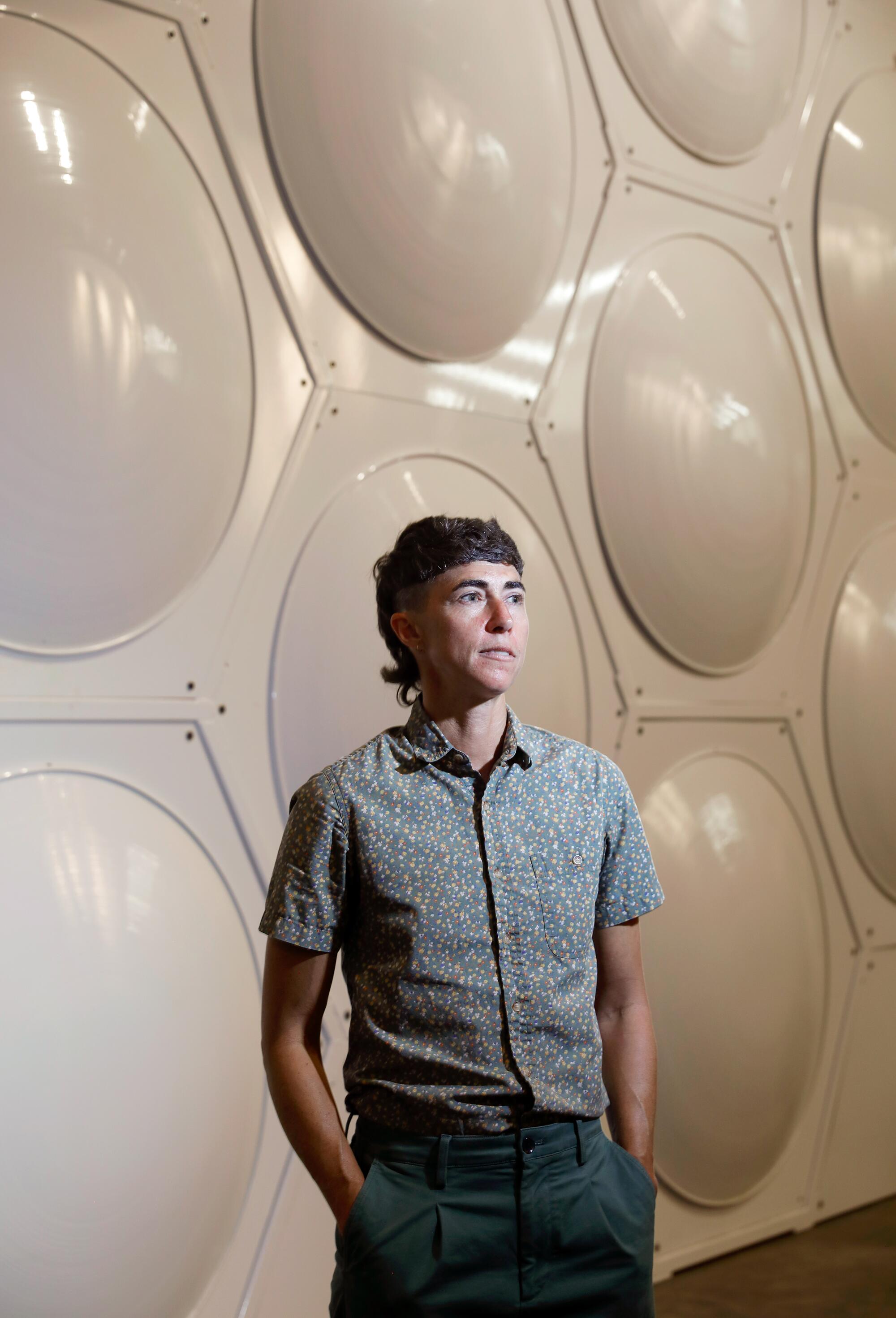 Katrina Spade stands in front of a white wall that looks like a honeycomb grid 