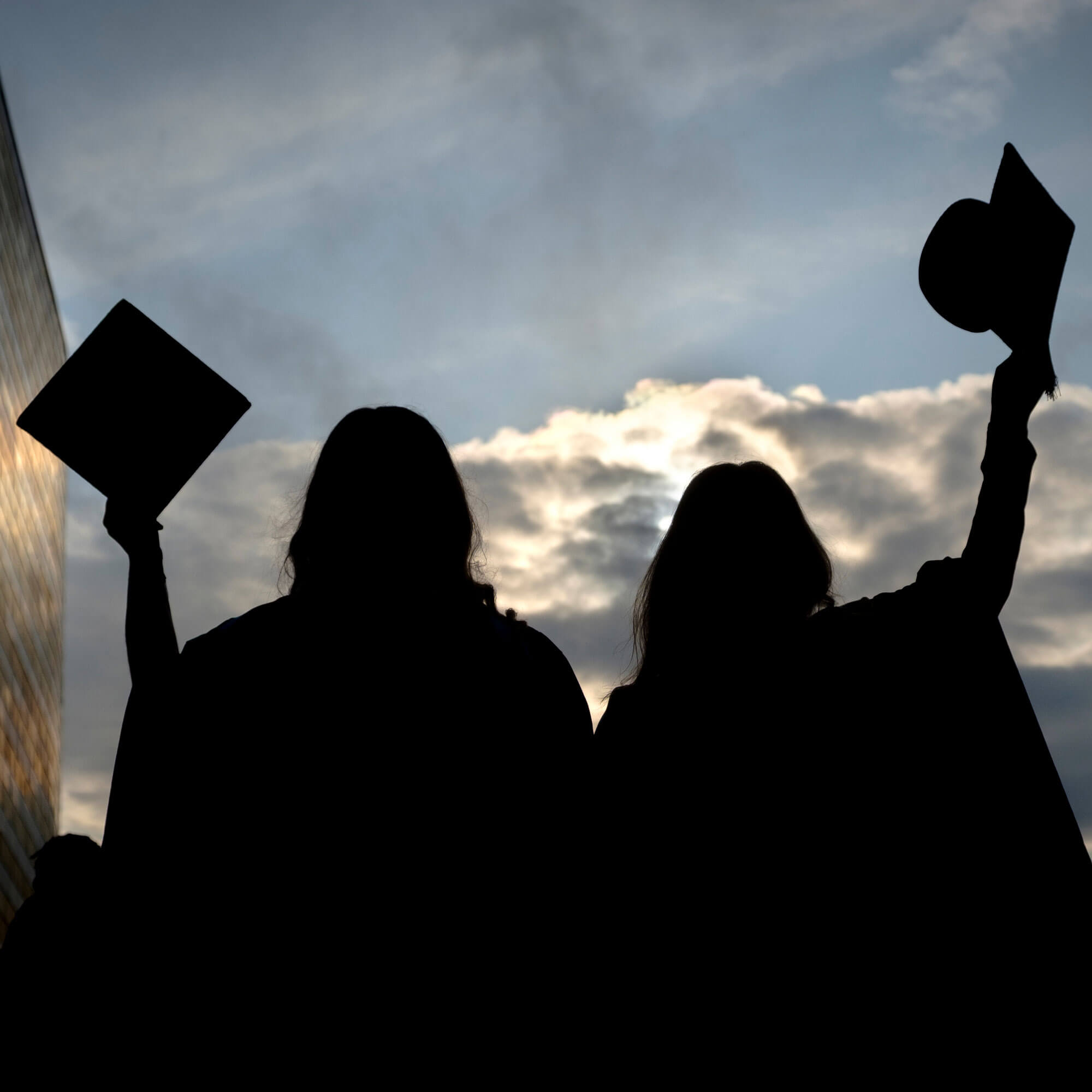 Silhouette of graduates raising mortar board hats in the air