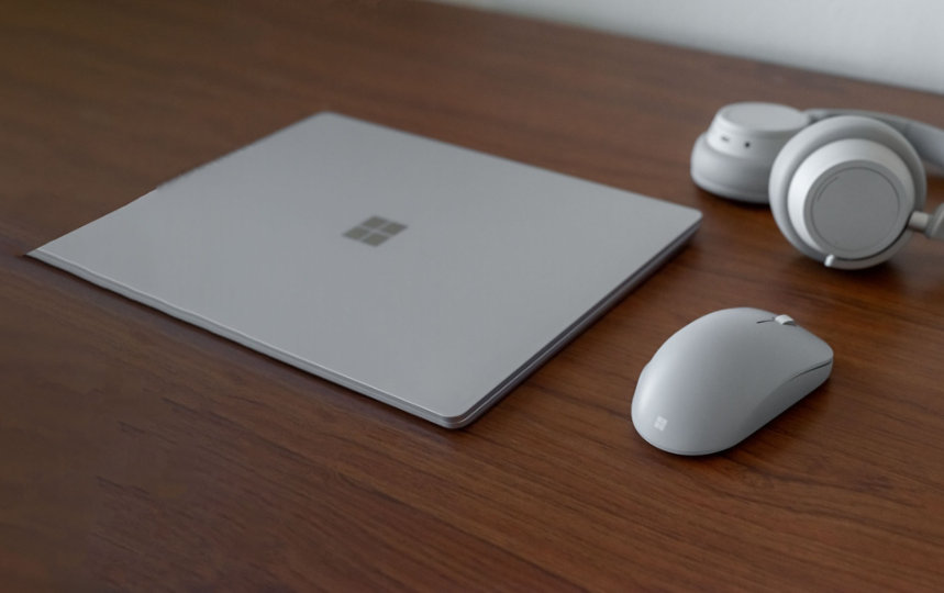 A Surface laptop, mouse, and headphones on a desk.