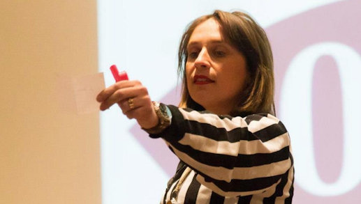 Severine Guilliet in a black and white striped with an outstretched arm holding a small piece of paper