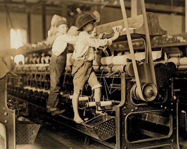 Young boys working in a thread spinning mill in Macon, Georgia, 1909. Boys are so small they have to climb onto the spinning frame to reach and fix broken threads and put back empty bobbins. Child labor. Industrial revolution