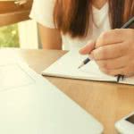 Student sitting at a desk with notebooks and a laptop studying for her SAT.