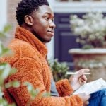 A student sits on a bench holding a pen and paper, studying to take the ACT.