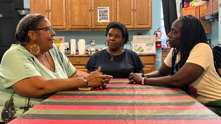 Three women sit a table talking. 