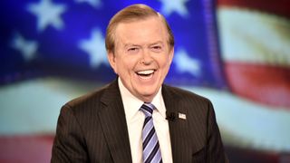 a man in a suit smiles on a tv set