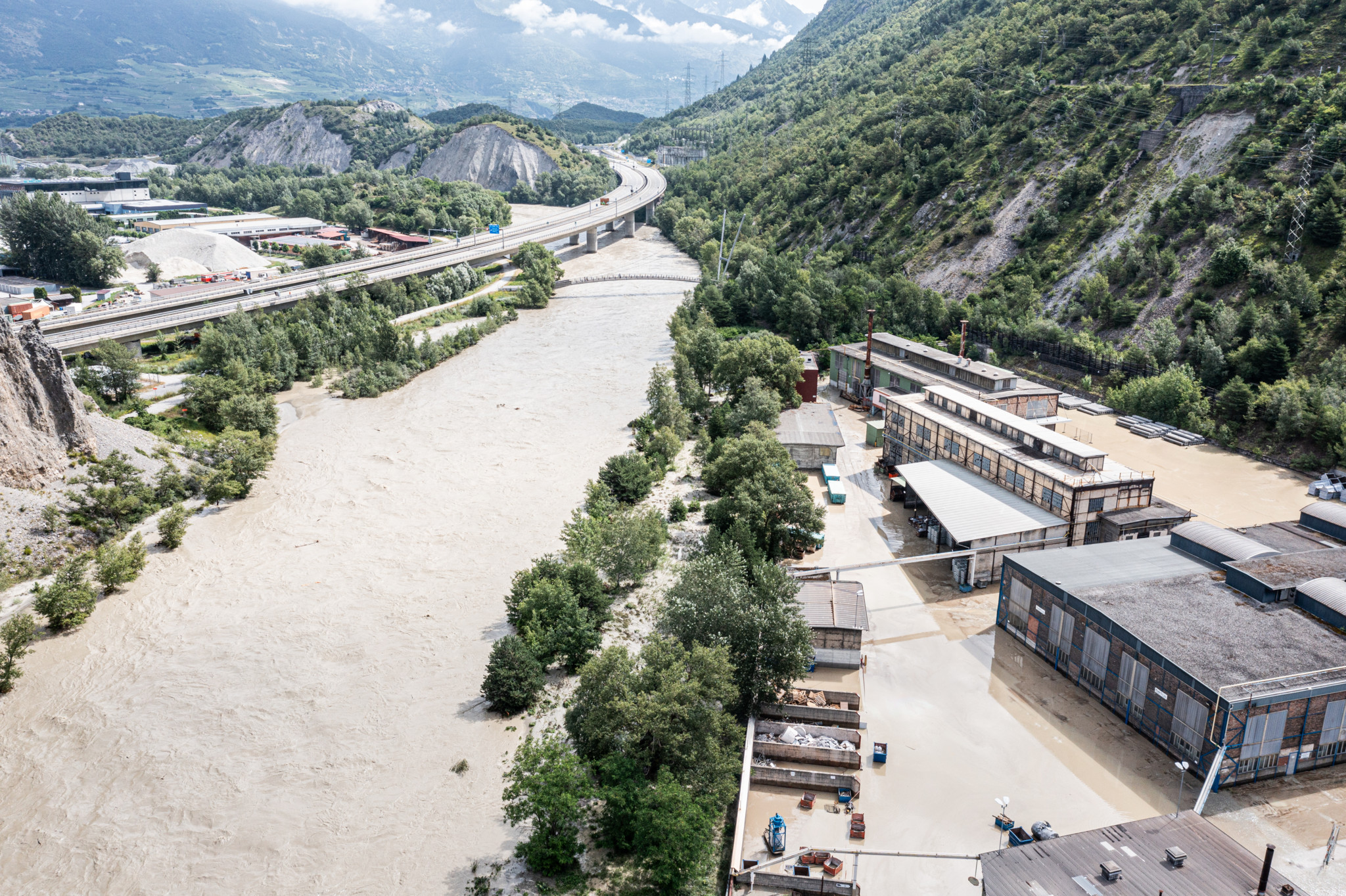 The Rhone River, left, and the Navizence river, are overflowing in the industrial zone produces aluminium "Constellium" following the storms that caused major flooding, in Chippis, Switzerland, Sunday, June 30, 2024. (KEYSTONE/OLIVIER MAIRE)
