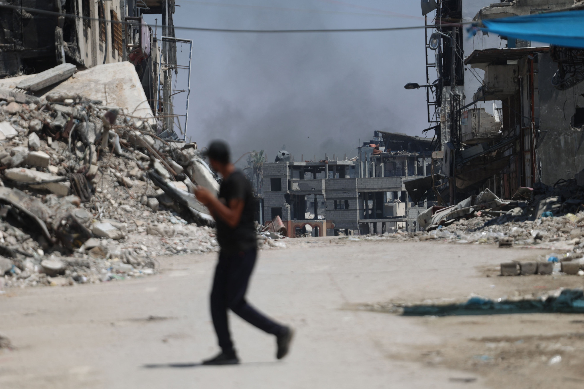 A Palestinian man crosses a street with smoke billowing in the background from an area targeted by Israeli bombardment in the Gaza City district of Shujaiya on June 28, 2024, amid the ongoing conflict between Israel and the militant Hamas group. Israel's military said on June 28 it was conducting raids backed by air strikes in northern Gaza, killing "dozens" of militants in an area where it had declared the command structure of Hamas dismantled months ago. The operation in Shujaiya, on the edge of Gaza City, caused numerous casualties, witnesses and medics said the previous day when it began. (Photo by Omar AL-QATTAA / AFP)