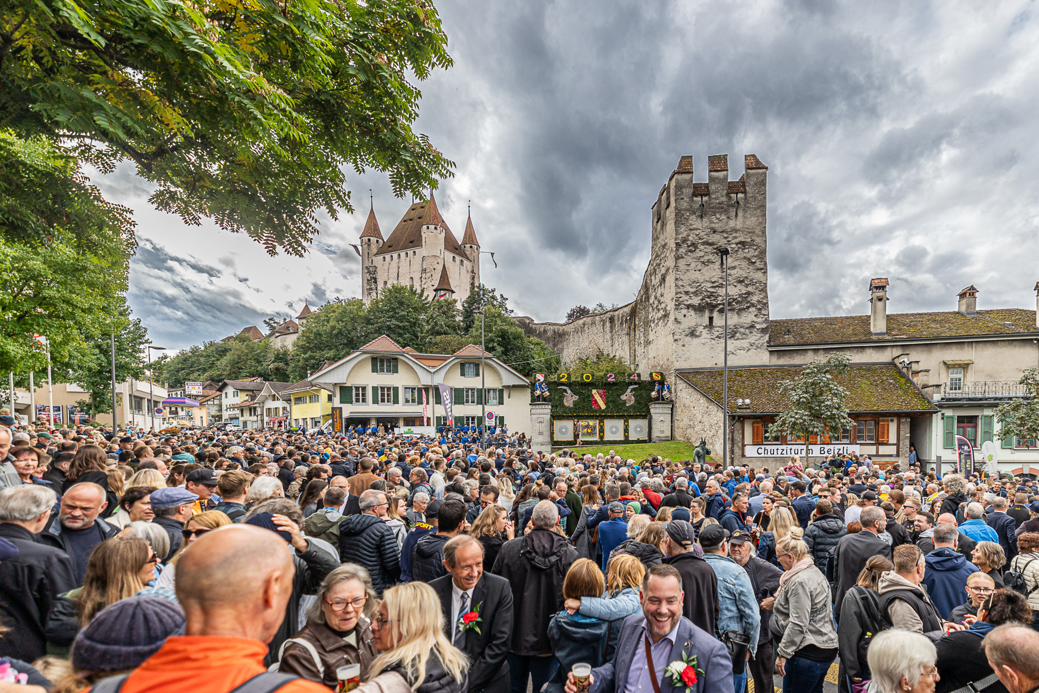 Menschenmenge beim Gesslerschiessen am Ausschiesset 2024 vor einer historischen Burg unter bewölktem Himmel versammelt.