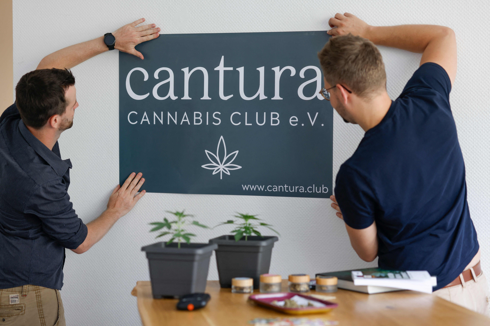 Fabian Baumann (R) chairman of the further cannabis club "Cantura e.V." and a colleague stick their association's name on the wall on June 28, 2024, in Munich, southern Germany, as so-called cannabis clubs will be allowed to sell the drug legally in Germany from July 1, 2024, but in practice it will be some time before the associations get up and running. Germany legalised cannabis in April 2024, allowing adults to carry 25 grams and cultivate up to three marijuana plants at home. As the next step in the reform, from July 1 it will be possible to legally obtain weed through "cannabis clubs" in the country. (Photo by Michaela STACHE / AFP)