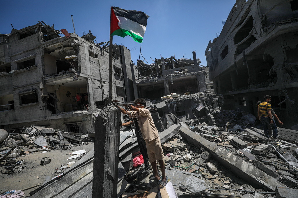 Un Palestinien met un drapeau de la Palestine parmi les décombres